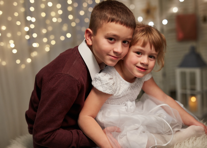 Young boy and girl sitting down with white lights behind them.
